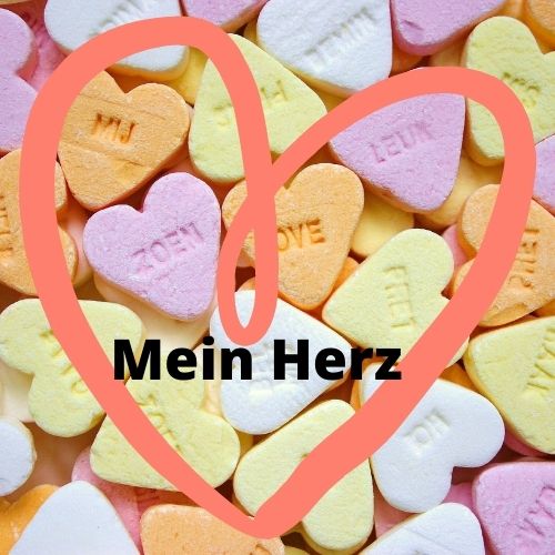 Es sind bunte Zuckerherzen zu sehen ein rotes Herz ist darüber gemalt und in diesem steht der Text meine Herz